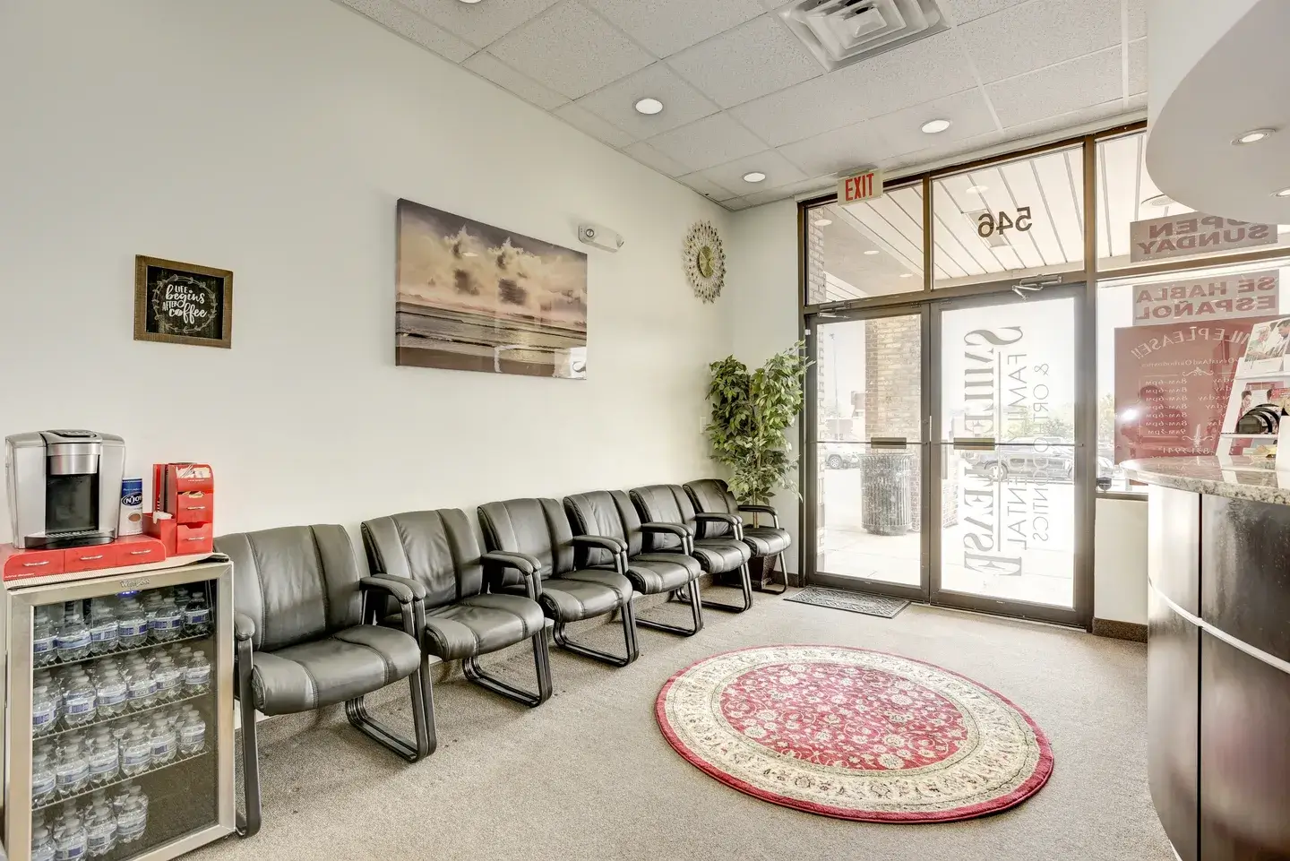 Empty waiting room with black chairs and a round rug near the door.